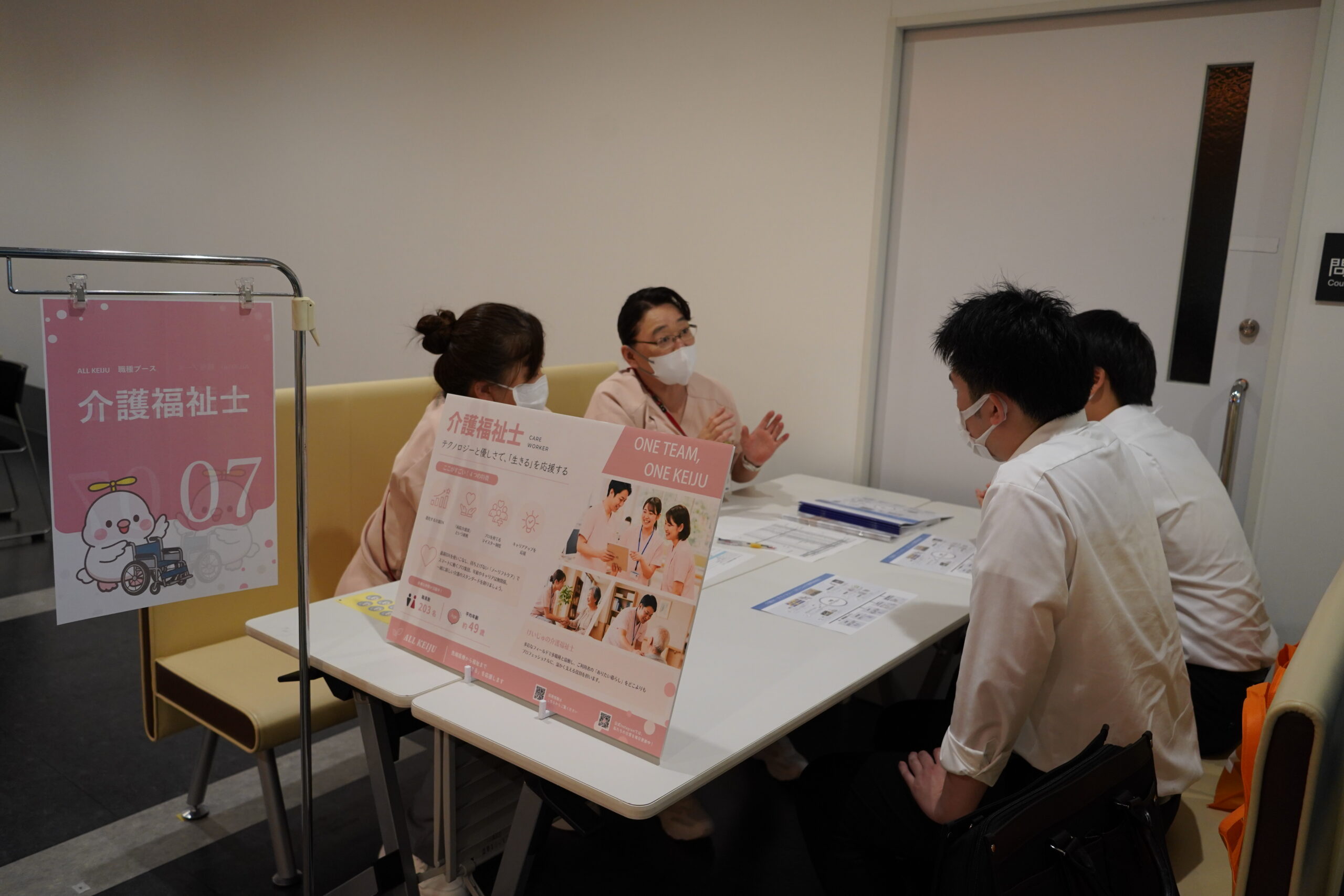介護福祉士ブースで、ピンクの案内パネルを前に職員が参加者へ説明している様子