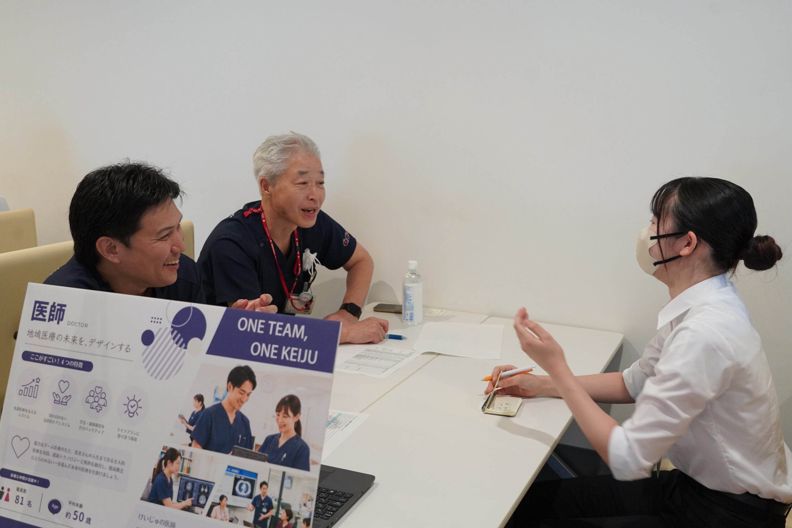 医師ブースで、笑顔の医師が身ぶりをまじえて参加者に話している様子