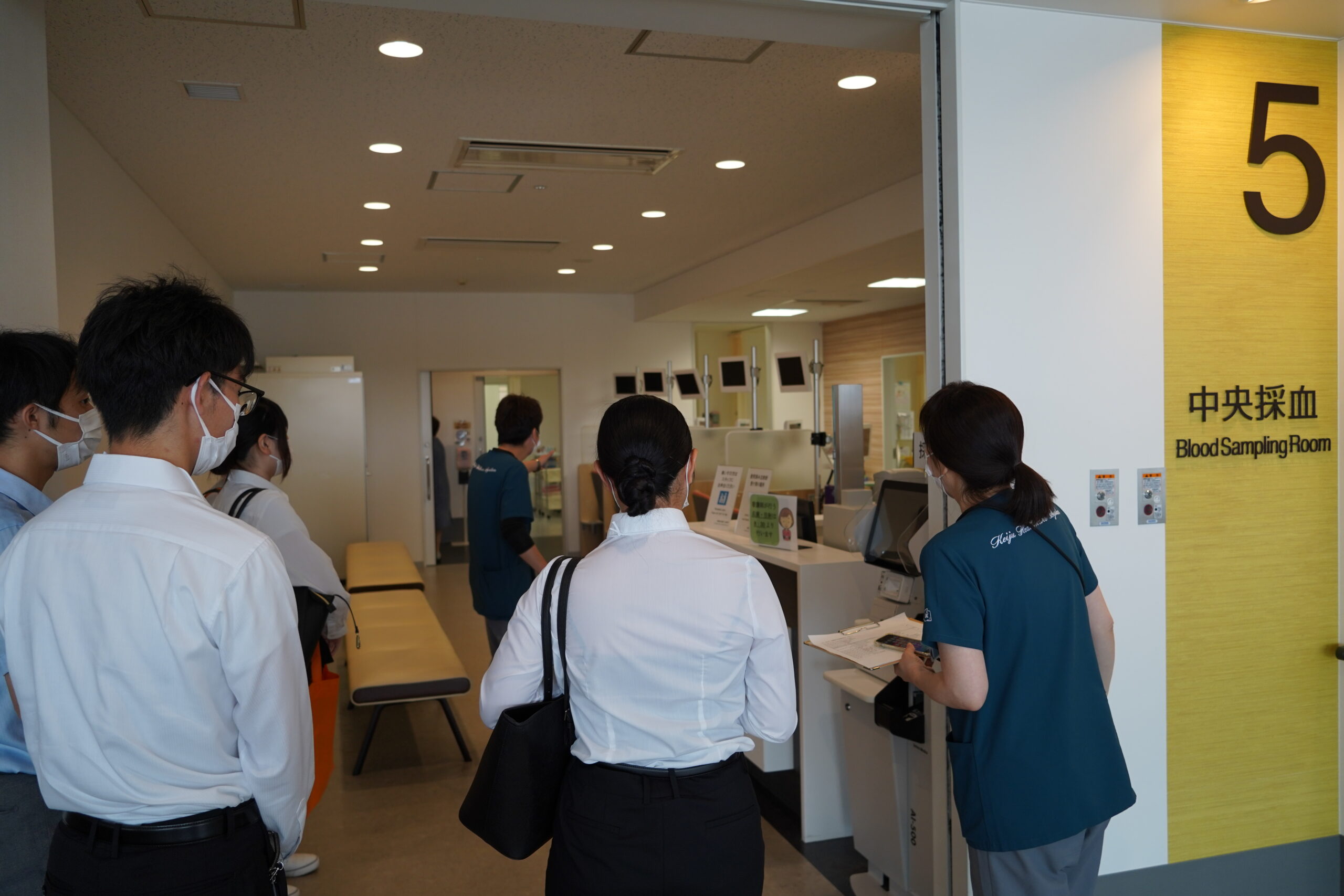 中央採血室の前で、職員の説明を聞きながら院内見学ツアーに参加している人たち