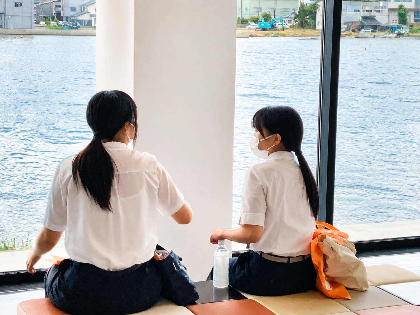 七尾湾を一望する窓辺の休憩スペースで、海を眺めながら座って休んでいる参加者2名